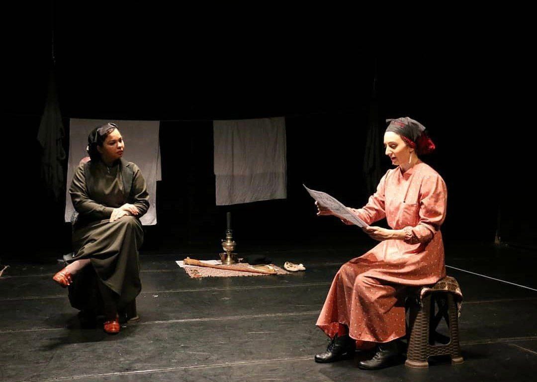 Two performers seated on a sparse stage