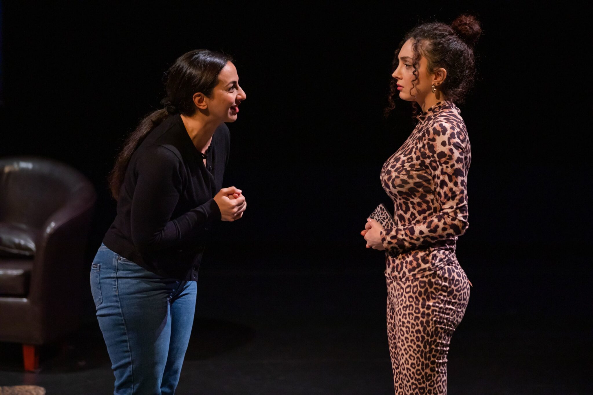 Two actors face one another on a dark stage